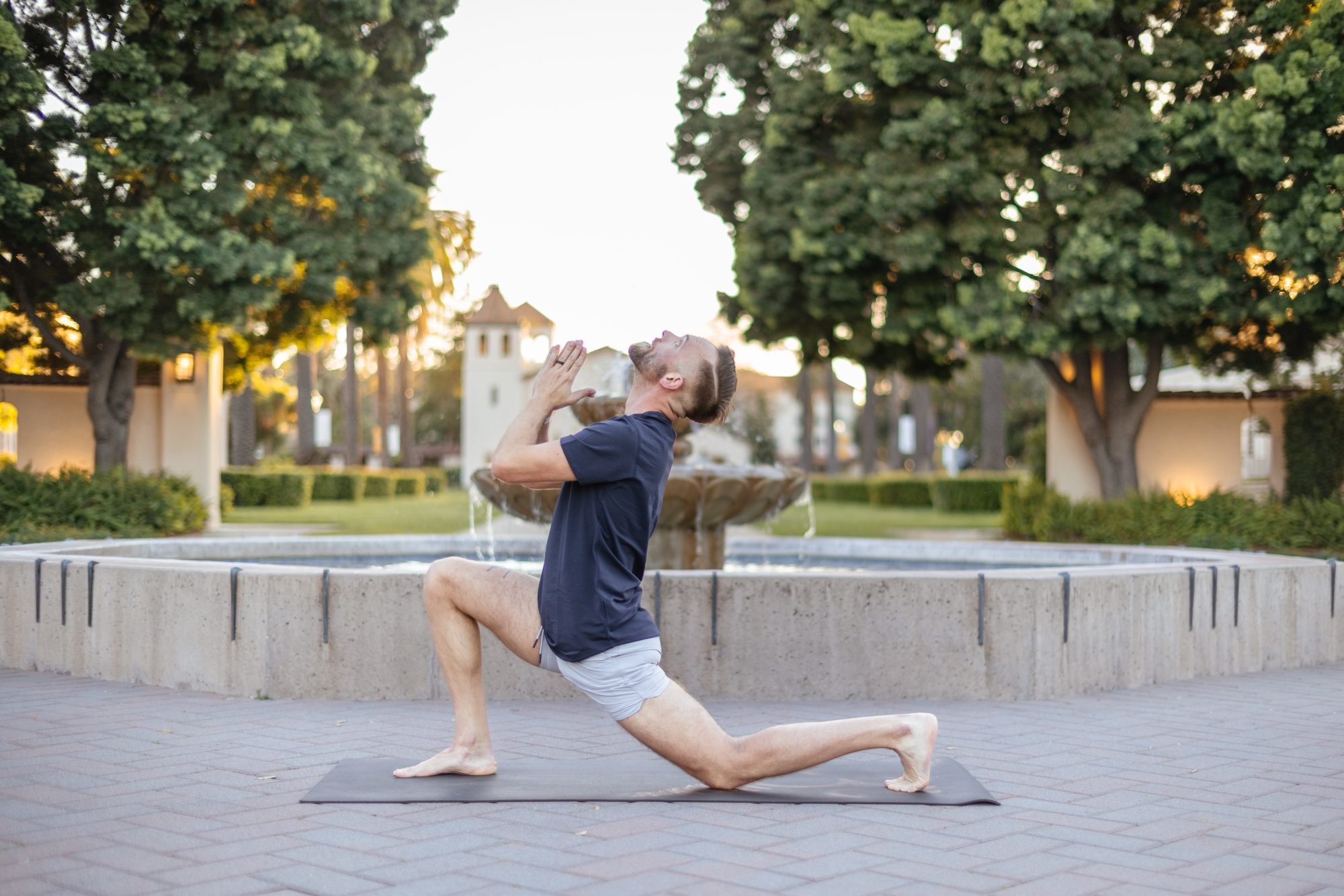 Bart in a low lunge on a yoga mat beside a fountain